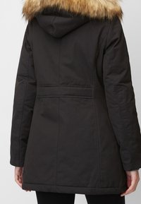Černá zimní bunda s kapucí a umělým kožíškem. Má hladkou texturu a svislé švy. Středně dlouhý design.