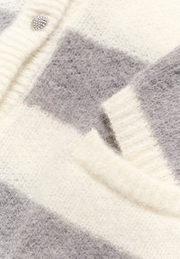 Cardigan in lana con strisce crema e grigie, polsini a costine e un bottone con strass. Tessuto morbido con una finitura pelosa.
