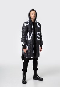 Długie czarne puchowe płaszcz z dużymi białymi literami, z przodu na zamek, z kapturem. Noszony na czarnym stroju, połączony z czarnymi botkami za kostkę.