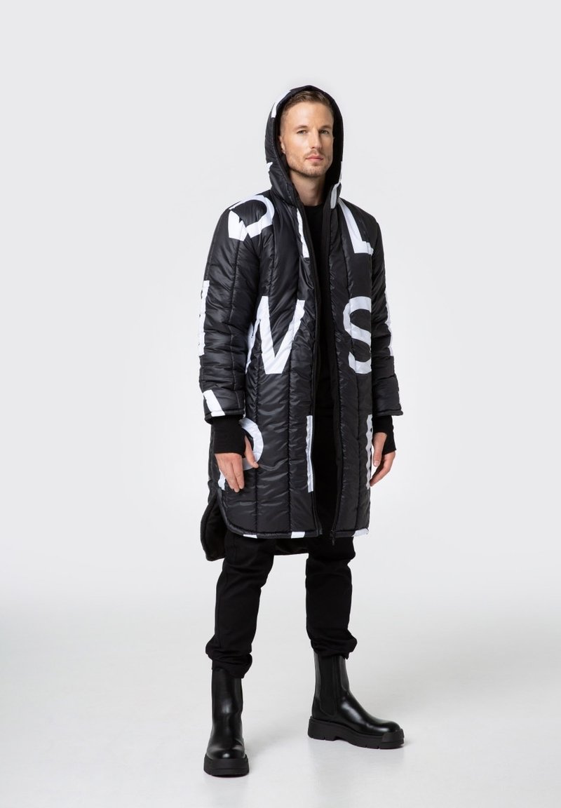 Długie czarne puchowe płaszcz z dużymi białymi literami, z przodu na zamek, z kapturem. Noszony na czarnym stroju, połączony z czarnymi botkami za kostkę.