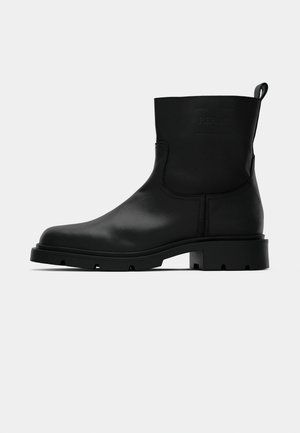 Schwarze Lederstiefel bis zur Mitte der Wade mit runder Zehe, flacher Profilsohle, Zugschlaufe auf der Rückseite und dezent geprägtem Branding am Schaft.