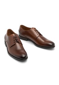 Zapatos de vestir de cuero marrón con un acabado suave, punta afilada, cordones en la parte delantera y una suela de goma negra. Diseño clásico adecuado para vestimenta formal.