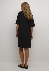Abito nero oversize con maniche corte, realizzato in tessuto morbido. Presenta spacchi laterali all'orlo per facilitare i movimenti. Design minimalista.