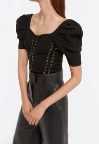 Top nero a maglia con maniche a palloncino, scollatura quadrata e accenti di hardware dorato sul davanti. Abbinato a pantaloni di pelle nera a vita alta.