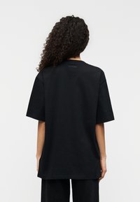 Μαύρο βαμβακερό T-shirt με άνετη εφαρμογή, κοντά μανίκια και στρογγυλή λαιμόκοψη. Φέρει τη λέξη «GUESS» σε μικρό εκτυπωμένο σχέδιο στην πλάτη.