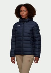 Jūras zila pūkainā jakas ar vertikālu quilting dizainu, priekšējo rāvējslēdzēju un kapuci. Iespējas ietver logotipu kreisajā krūtīs un uzlīmi uz piedurknes.