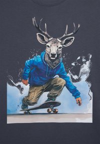Grafisches T-Shirt mit einem Skateboardfahrer mit einem Hirschkopf, der einen blauen Hoodie und beigen Hosen trägt. Der Hintergrund enthält Spritzeffekte in Blau und Weiß.