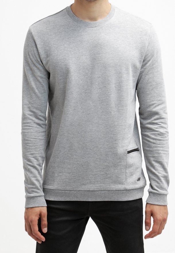 Homme portant un sweat-shirt uni gris clair à manches longues avec une petite poche zippée en bas à l'avant, associé à un pantalon noir.