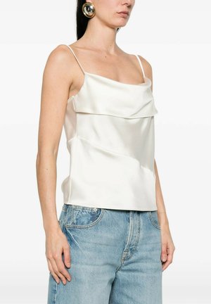 Donna che indossa una canottiera di raso bianca con spalline sottili, abbinata a jeans a vita alta di colore azzurro chiaro e un grande orecchino rotondo dorato.