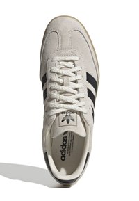 Chaussure de sport en daim gris clair avec des rayures noires. Présente un upper texturé, des lacets plats et une semelle intérieure rembourrée. Silhouette classique.
