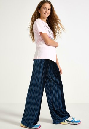 Jasnoróżowa bawełniana koszulka z graficznym nadrukiem w połączeniu z granatowymi, w paski, szerokimi spodniami z weluru. Całość dopełniają niebiesko-żółte trampki.