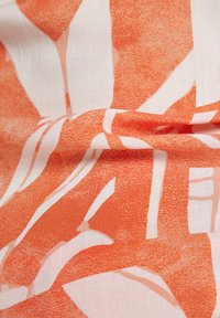 Baumwollstoff mit einem auffälligen orange-weißen, abstrakten Blattmuster, das texturierte Details und eine weiche, glatte Oberfläche aufweist.