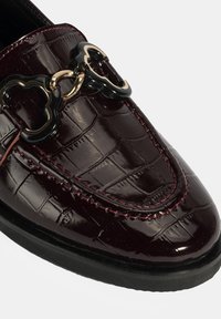 Bordeaux lakleren instapper met krokodillenstructuur, featuring een gouden en zwarte hartvormige schakel detail en contrasterende stiksel.