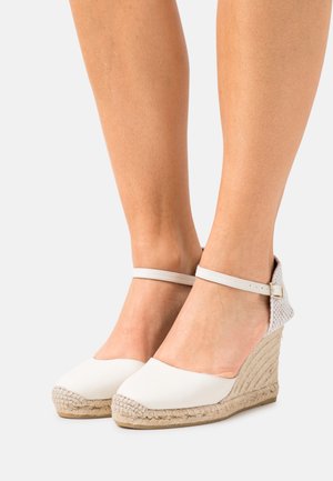 Espadrilles blanches à semelle en jute tissé, avec une tige en toile lisse et une fine sangle de cheville avec une boucle en métal.