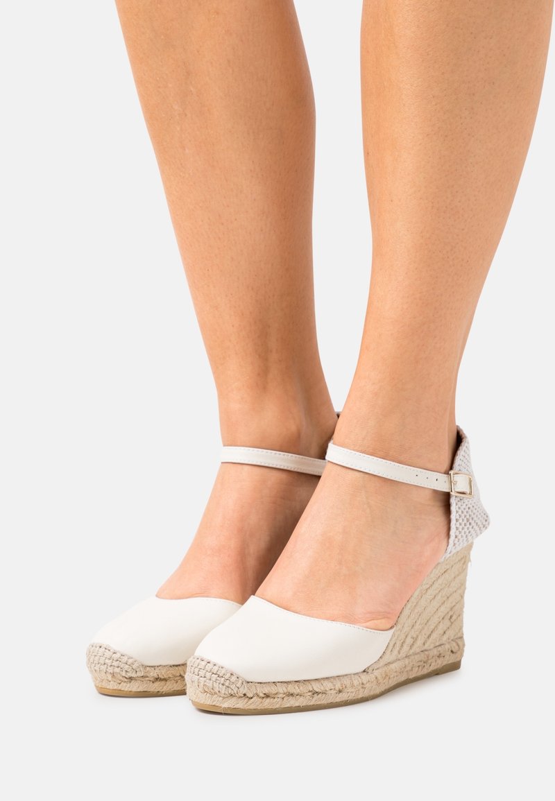 Espadrilles blanches à semelle en jute tissé, avec une tige en toile lisse et une fine sangle de cheville avec une boucle en métal.