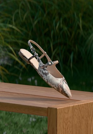 Spisse slingback-flats laget av teksturert slangeskinnlær, med doble stropper og metallspenner, som hviler på en treoverflate.