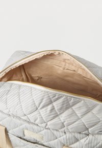 Ριγέ καπιτονέ σακίδιο με ανοιχτό μπεζ φερμουάρ που αποκαλύπτει εσωτερική θήκη με φερμουάρ και υφασμάτινη επένδυση.