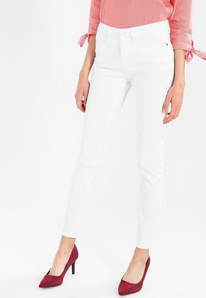 Weiße enge Jeans aus Denim, mit einem klassischen Fünf-Taschen-Design und einer mittelhohen Taille, kombiniert mit einem rot gestreiften Oberteil und burgunderfarbenen Absätzen.