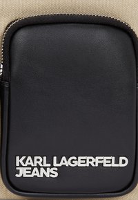 Black leather pouch with a zip closure, featuring silver "KARL LAGERFELD JEANS" text. Background is a light beige fabric.