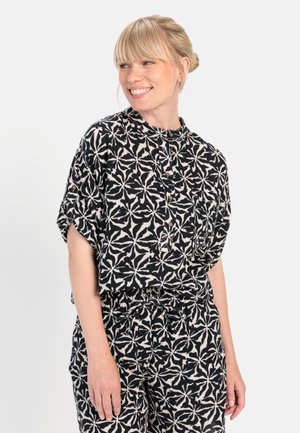 Sort og creme mønsteret bluse med afslappet pasform, korte ærmer og høj hals. Har knapdetaljer langs fronten og en løs, luftig tekstur.