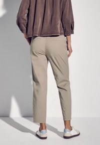 Beiga, avsmalnande bombyxor med två bakfickor, som kombineras med vita skor med blå detaljer. Tyget ser slätt och lätt ut.