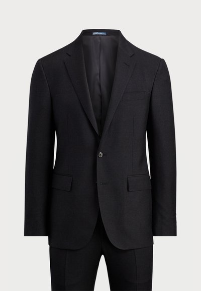 Tumši pelēkās vilnas uzvalks ar divu pogu priekšpusi, izgrieztiem apmali, kabatas ar atloku un šauru piegriezumu. Iezīmē gludu iekšējo oderi.