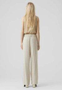 Beżowy top bez rękawów w zestawieniu z jasnoszarymi spodniami w stylu szerokich nogawek, które mają elastyczny pas i dwie tylne kieszenie. Gładka tekstura materiału.