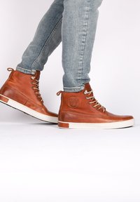 Zapatos de cuero marrón de caña alta con superficie texturizada, suela de goma blanca y cordones grises, exhibidos con pantalones vaqueros.