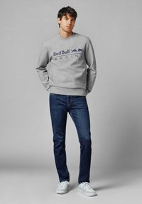 Sudadera gris con logo de "Red Bull Racing" en navy, combinada con jeans oscuros y zapatillas blancas. Diseño sencillo, material de algodón.