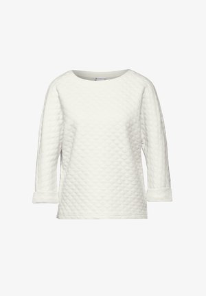 Haut blanc matelassé à manches longues avec un col rond et des poignets repliés, présentant un motif texturé en losanges sur l'ensemble.