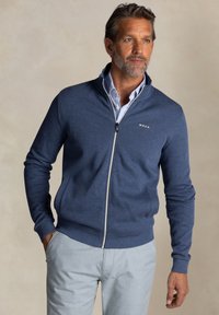 Navyblauwe zip-up trui van zachte stof met geribde mouwen en onderkant, met een klein logo op de linkerborst en zijzakken.