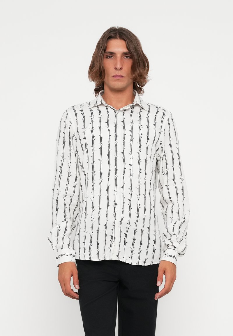 Camisa de manga longa em tecido branco com estampado botânico preto. Apresenta colarinho com botões e corte descontraído. Textura suave e leve.