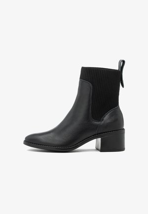 Stivaletto in pelle nera con tomaia in tessuto a coste, tacco a blocco, punta arrotondata e linguetta per il pull su sfondo bianco.