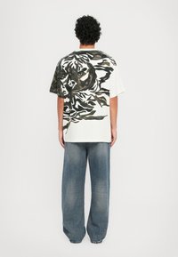 White short-sleeve t-shirt with a large black and green tiger graphic on the back. Paired with loose-fitting light blue denim jeans.