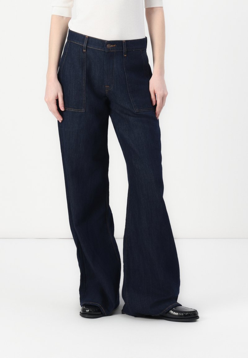 Mørkeblå denim bukser med vide ben som har høy midje, frontlommer og kontrast-søm. Glatt tekstur, uformelt design.