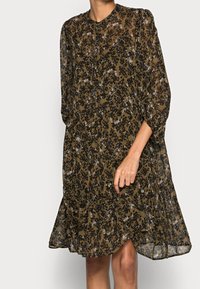 Brun blommig klänning i genomskinlig tyg, har rund halsringning, långa puffärmar och en utsvängd kjol med en flödande silhuett.