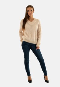 Suéter beige de cuello en V, con textura de punto, de corte relajado. Combinado con jeans de denim en azul oscuro, de corte slim, y tacones negros de punta.