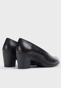 Zapatos de tacón alto de cuero negro con puntera redondeada y tacón grueso. Textura suave, mínima marca en la parte trasera, diseño sencillo.