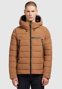 Smeđi puffer kaput s kapuljačom, s horizontalnim quilted dizajnom, zatvorenim džepovima s patentnim zatvaračem i kontrastnim crnim patentnim zatvaračima. Crni logo na prsima.