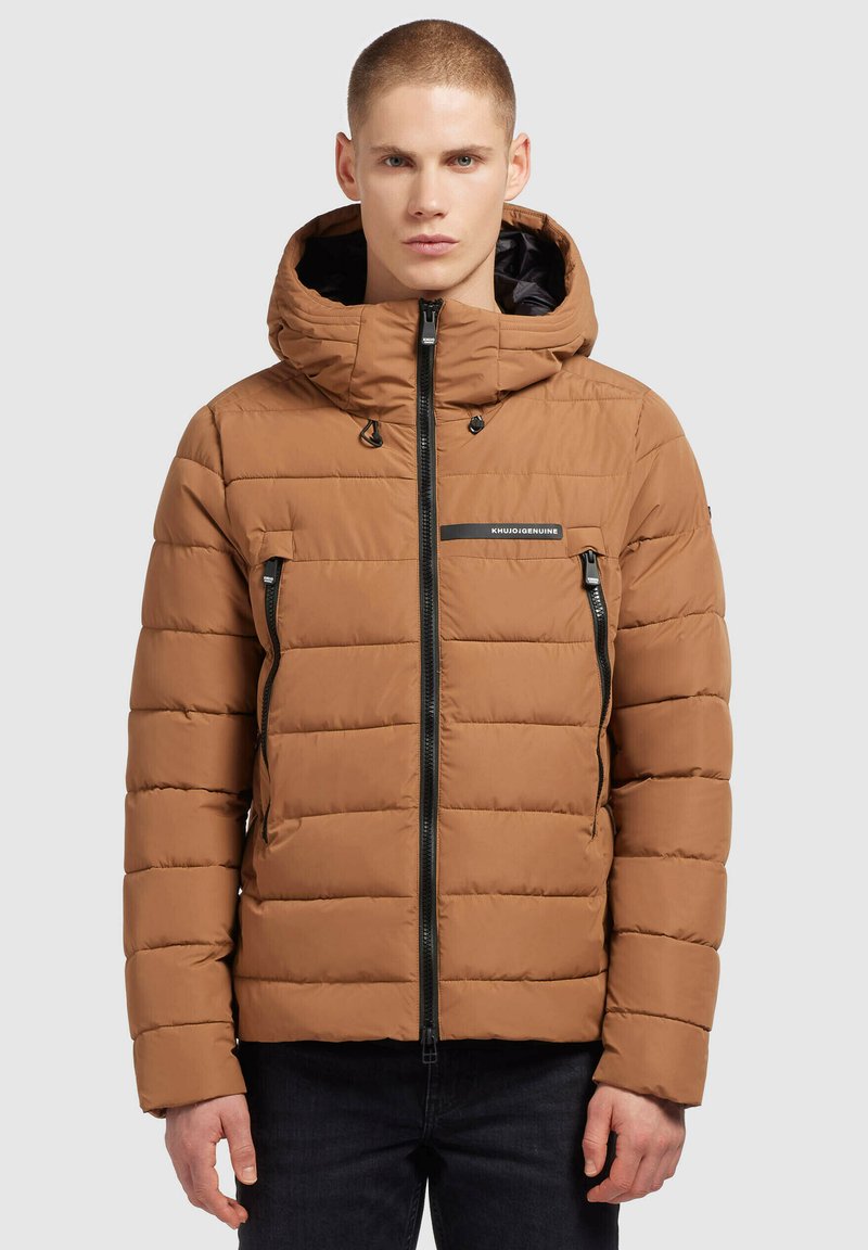 Smeđi puffer kaput s kapuljačom, s horizontalnim quilted dizajnom, zatvorenim džepovima s patentnim zatvaračem i kontrastnim crnim patentnim zatvaračima. Crni logo na prsima.