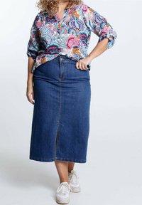 Blouse à imprimé floral avec des manches courtes retroussées, associée à une jupe en denim mi-longue avec une fente avant et un fermeture à boutons métalliques. Baskets blanches.