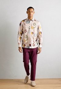 Long-sleeve button-up shirt with a light pink fabric featuring colorful floral and abstract patterns, paired with burgundy fitted pants.