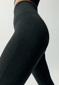 Czarne legginsy sportowe z fakturą ryfle, wysokim stanem oraz dopasowanym krojem, który podkreśla kształt i zapewnia wsparcie.