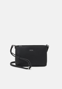 Svart läder crossbody-väska med slät yta, en justerbar rem och dragkedjestängning. Har en diskret logotyp framtill.