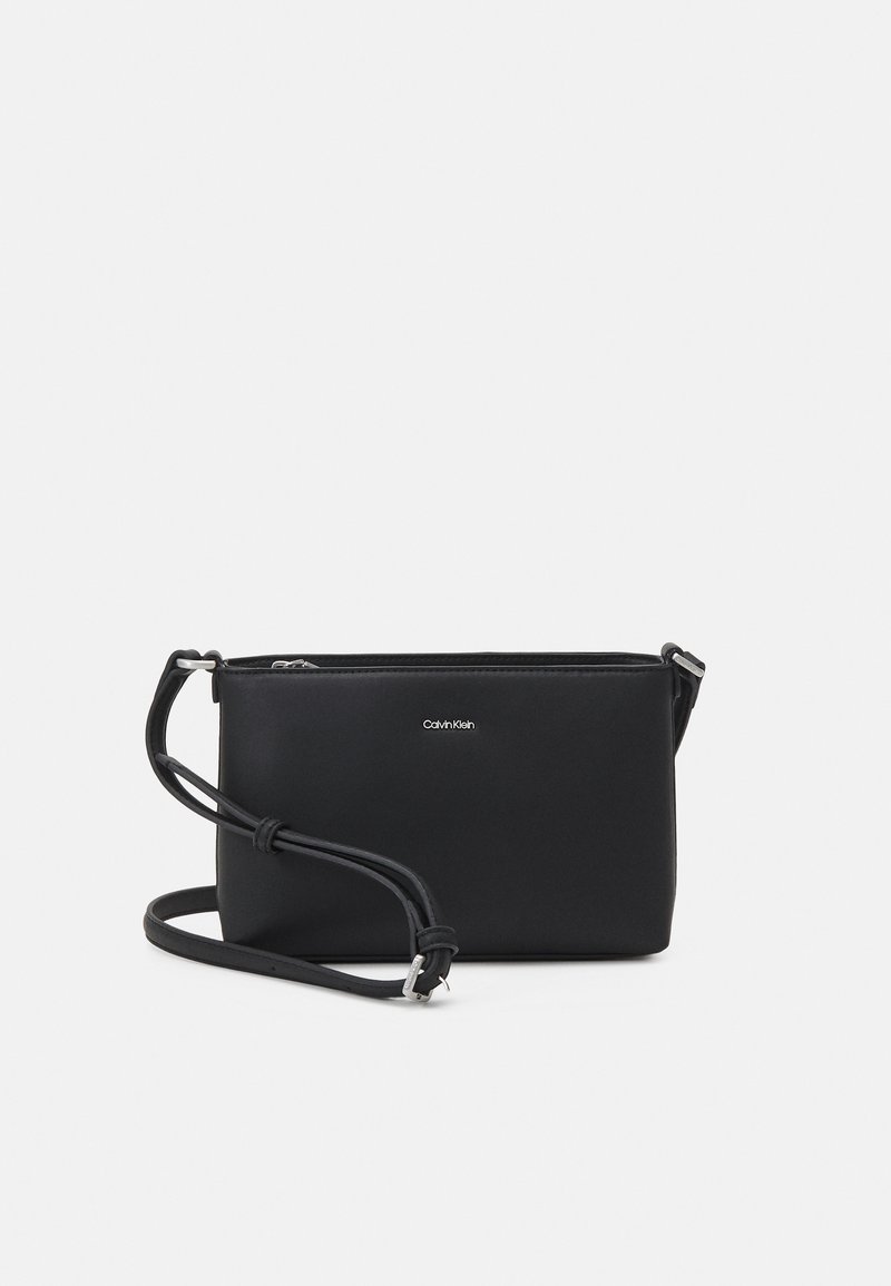 Svart läder crossbody-väska med slät yta, en justerbar rem och dragkedjestängning. Har en diskret logotyp framtill.
