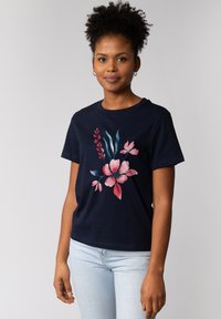 T-shirt en coton bleu marine avec imprimé floral rose et vert. Manches courtes et col rond. Silhouette cintrée. Jeans bleu clair.