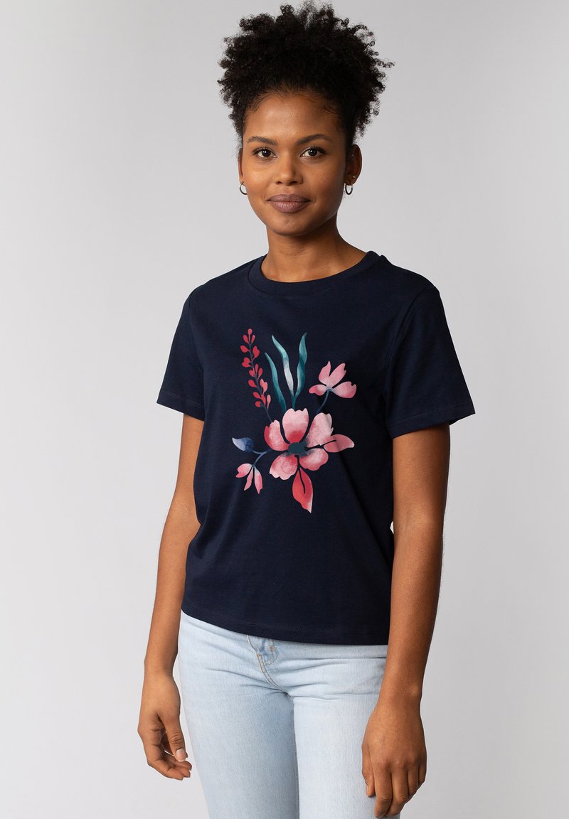 T-shirt en coton bleu marine avec imprimé floral rose et vert. Manches courtes et col rond. Silhouette cintrée. Jeans bleu clair.