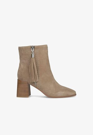 Botte de cheville en suède taupe avec un bout pointu, accents en clous argentés, fermeture éclair latérale et un détail en frange sur la tirette de la fermeture. Talon empilé en bois.