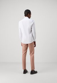 White long-sleeve shirt paired with light pink trousers. The shirt features a classic collar, and the model wears black shoes.