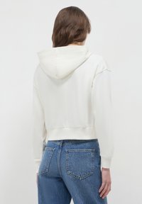 Sweat à capuche blanc coupé avec une large capuche, des poignets et un ourlet côtelés. Associé à un jean bleu taille haute avec des poches arrière et une texture délavée.